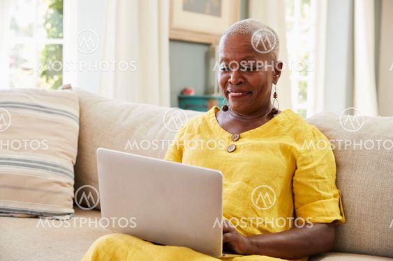 Senior Woman Sitting On Sofa Using Laptop At Home Together