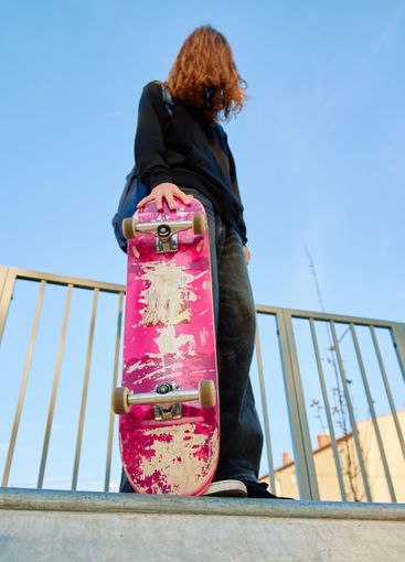 Skateboarder holding pink skateboard at skatepark