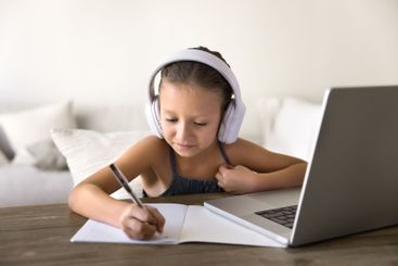 Cute little girl wear headphones studying online through...