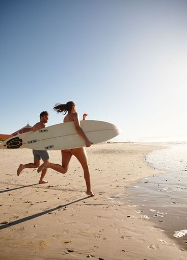 Surfing, couple and running on beach with blue sky,...