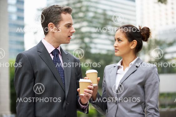 Businessman And Businesswoman Chatting In Street Holding Takeaway Coffee