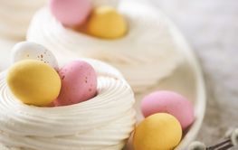 Easter meringue nests with colorful sweet eggs on plate.