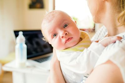 Unrecognizable mother holding baby son, milk in bottle,...