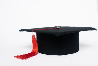 Black graduation cap with red tassel on white background