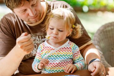 Young middle-aged father feeding cute little toddler...