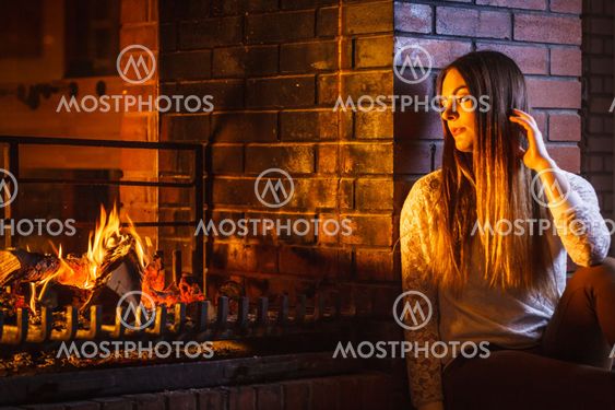Pensive woman relaxing at fireplace. Winter home.
