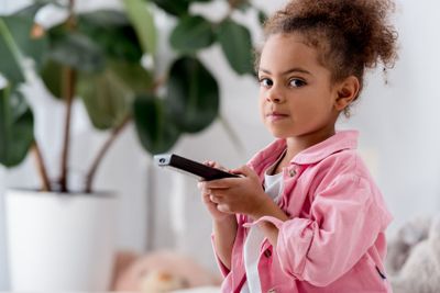  close up of African american child sitting with tv remote 
