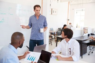 Three men discussing business at whiteboard in a busy...