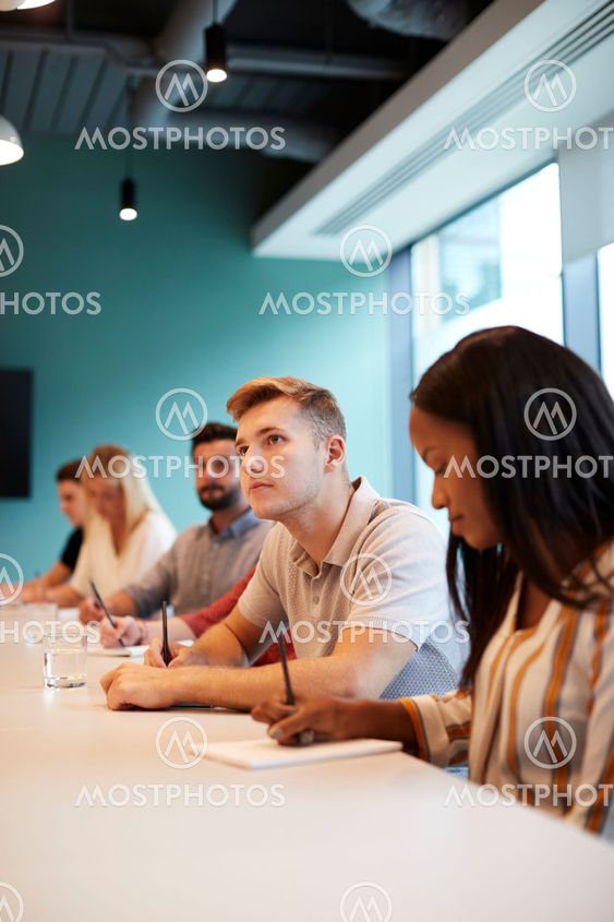 Group Of Young Candidates Sitting At Boardroom Table...