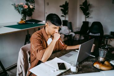 Thoughtful male business professional working on laptop...