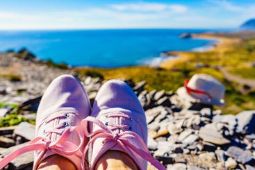 Female legs in sneakers against coast landscape, Spain.