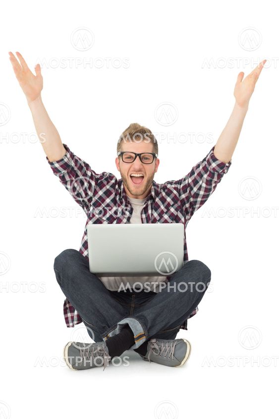 Handsome man cheering at camera with laptop sitting on floor