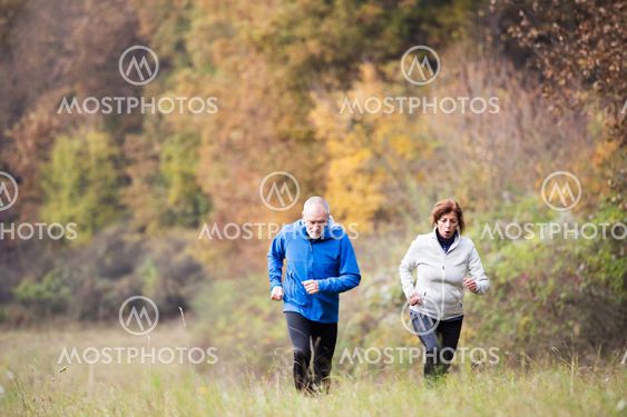 Beautiful senior couple running outside in sunny autumn...