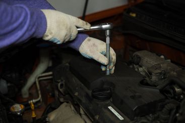 A gloved auto mechanic concentrates on using a ratchet...