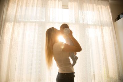 Portrait of cheerful mother holding her baby against big...