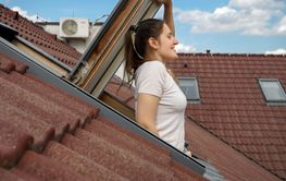Woman smiling while looking out of an attic window under...