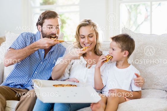 Parents and child sitting on sofa and having pizza
