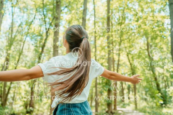 Happy woman in forest with open arms from behind...