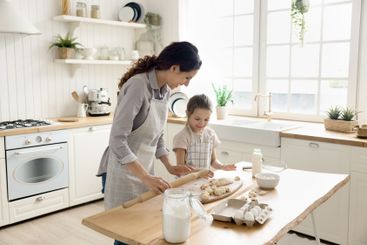 Happy young mom teach little daughter to knead roll dough