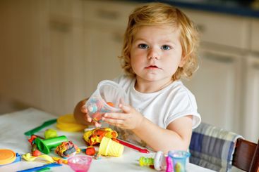 Adorable cute little toddler girl with colorful clay at...