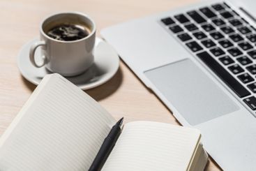 Cup of coffee beside an open notebook and laptop on a...