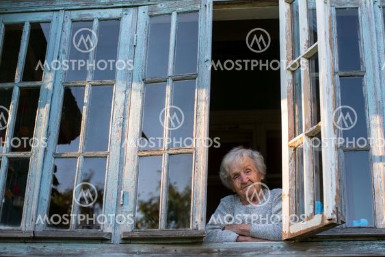 Grandmother, an elderly woman looks from the window of...