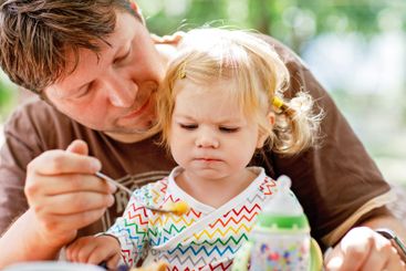 Young middle-aged father feeding cute little toddler...