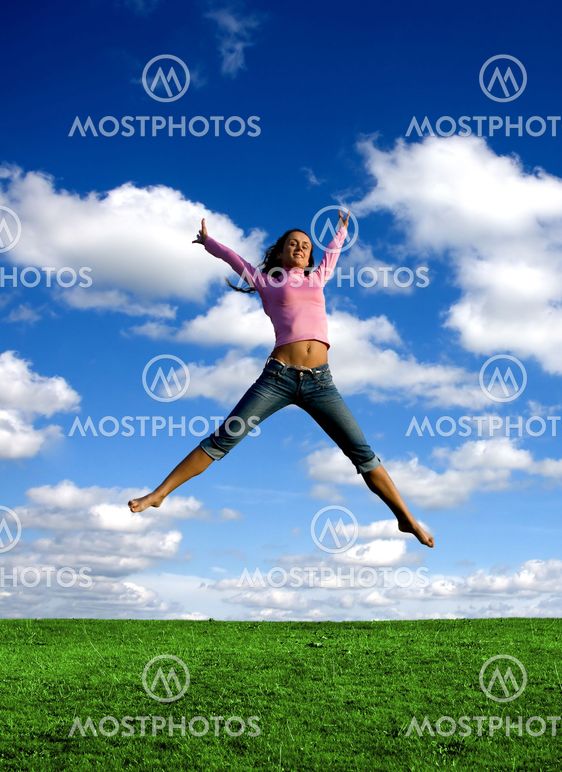 Happy young beautiful girl jumping in the green field.