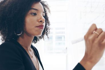 Black woman, writing and finance on board in office with...