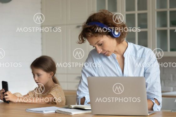 Modern day mother and daughter sit at desk use gadgets