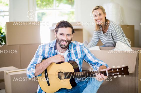 Man playing a guitar while woman unpackaging cardboard...