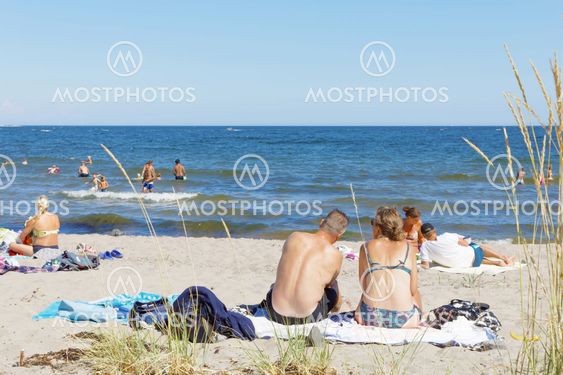 Sunbathing people relaxing on the sand beach, blue sky in...