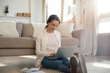 Smiling woman working from home sitting on floor holding...