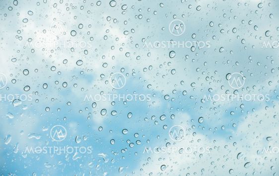 Drops of water on glass window over blue sky .