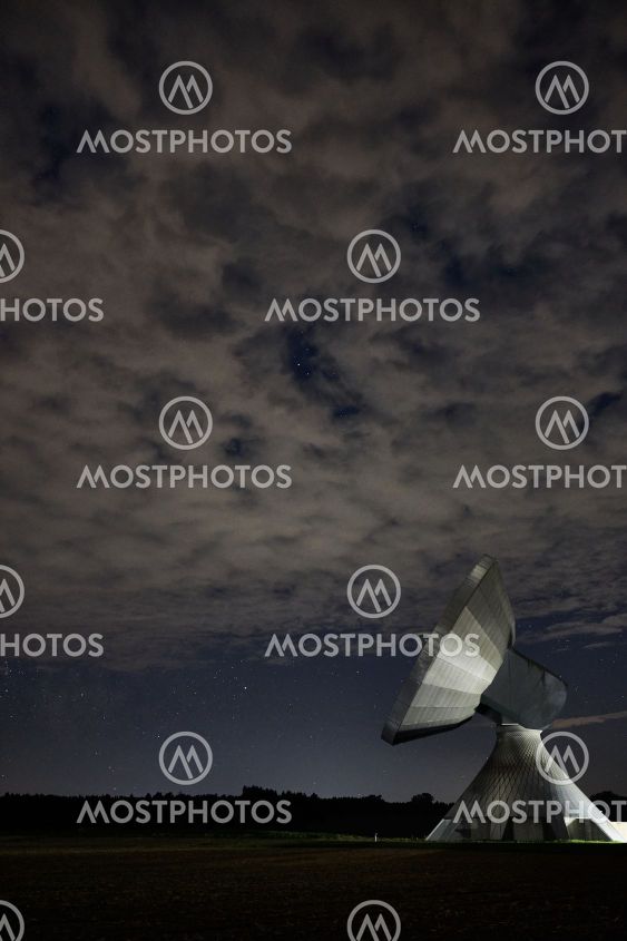 A dish antenna under a cloudy night sky