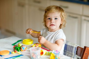 Adorable cute little toddler girl with colorful clay at...