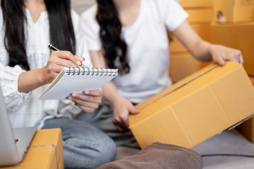 A close-up of two women preparing items for shipping to...