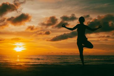 A woman practicing yoga on the seashore during a sunset