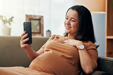 Pregnant woman, smile and selfie on sofa in home with...