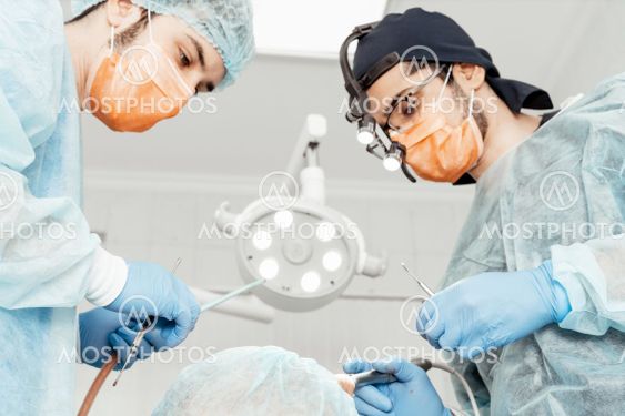 Two male dentists perform an operation on a patient....