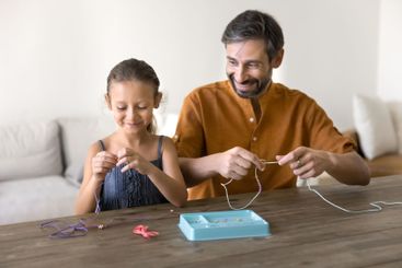 Father and little daughter making jewellery from beading...