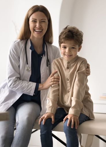 Young female pediatrician hugging little boy patient...