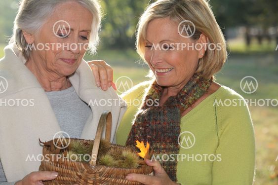 a mid age blonde woman and an older woman holding a wickerwork basket full of chestnuts