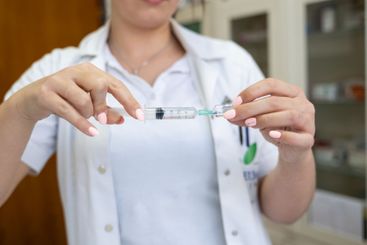 A focused nurse in a white lab coat carefully prepares a...