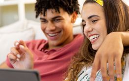 Happy diverse couple using tablet relaxing on sofa in living