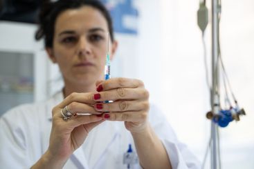 A focused nurse in a white lab coat carefully prepares a...