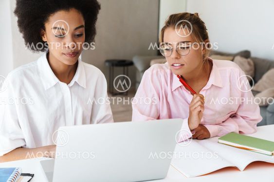 Focused multicultural students girls doing homework with...