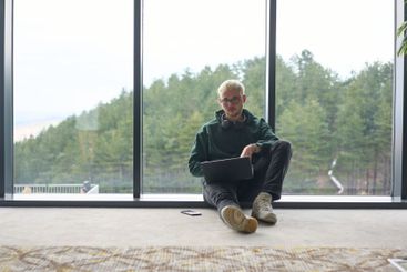 A blonde man sitting on the floor of a modern office,...