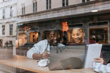 Happy female coffee shop owners discussing over laptop...