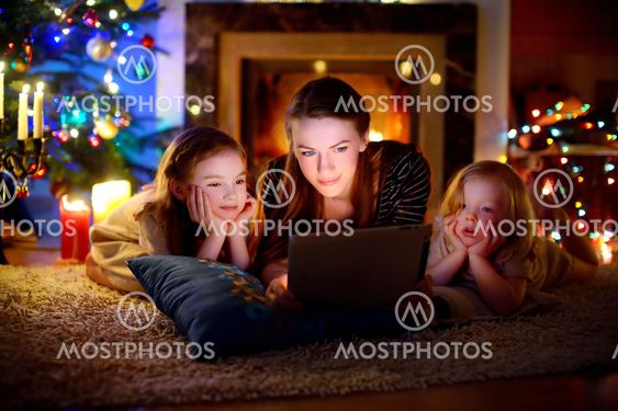 Mother and daughters using a tablet by a fireplace on...